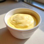 A close-up of thick, creamy, yellow hollandaise sauce served in a small white bowl.