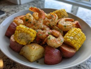 A close-up view of a bowl filled with seasoned shrimp boil ingredients, including plump shrimp, corn on the cob pieces, red potatoes, and sausage slices.