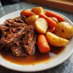 A serving of tender, shredded pot roast swimming in rich gravy alongside roasted carrots and potatoes.