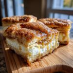 A close-up of three squares of sopapilla cheesecake drizzled with honey or syrup and coated in cinnamon sugar.