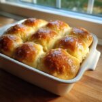 A close-up of eight golden brown sourdough discard rolls baked together in a white dish.