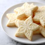 Close-up of several star-shaped vegan sugar cookies with embossed snowflake patterns, lightly dusted with sugar.