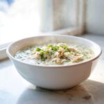 A steaming white bowl filled with creamy keto white chicken chili, topped with shredded chicken and fresh cilantro.