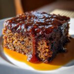 Close-up of a rich, dark square slice of sticky toffee pudding recipe drenched in thick toffee sauce.