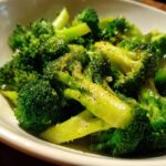 Close-up of vibrant green steamed broccoli florets tossed with garlic and pepper in a white bowl.