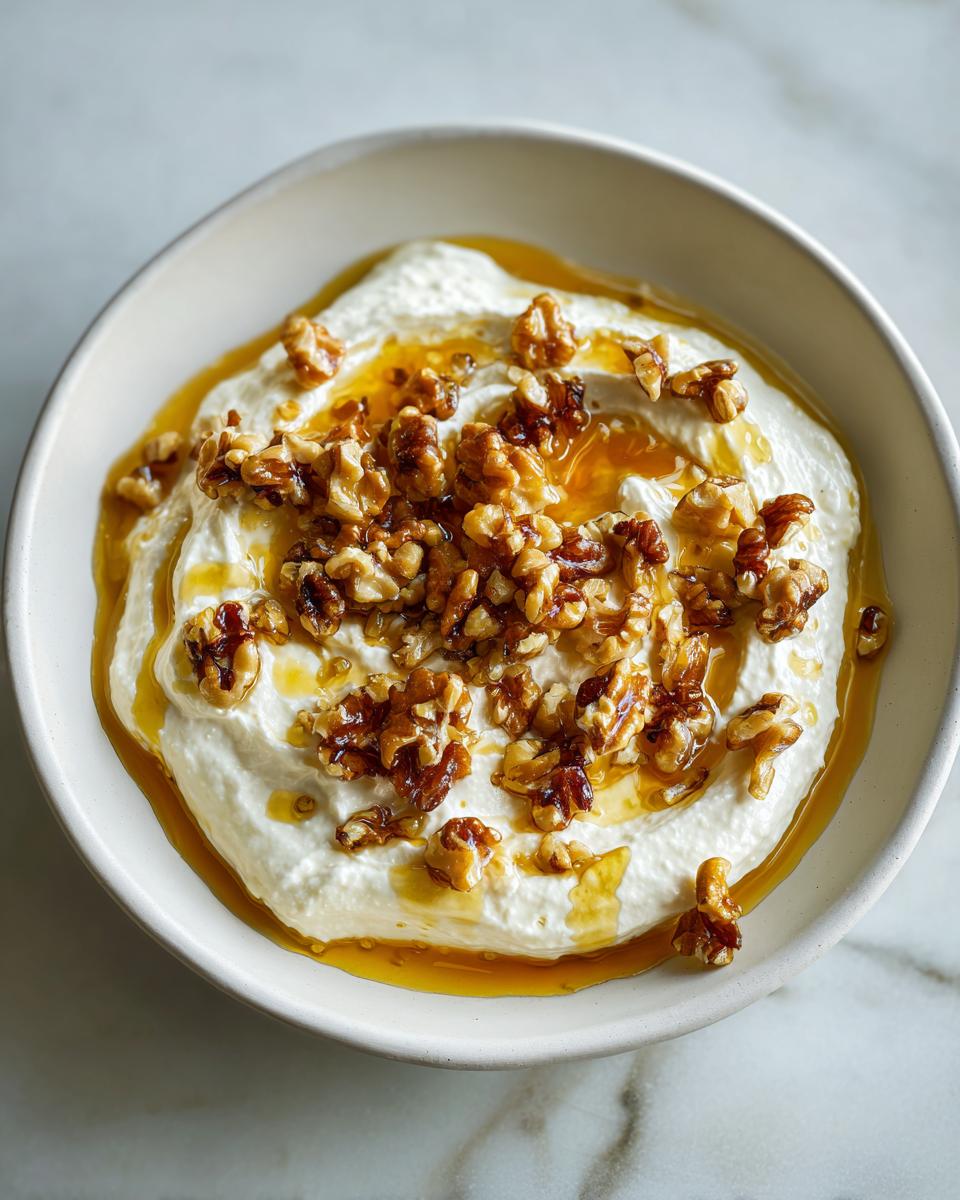 A bowl of creamy whipped ricotta dip drizzled with honey and topped with candied walnuts.