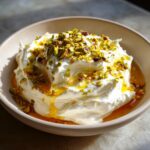 A close-up of a creamy, whipped ricotta dip drizzled with golden honey and topped with chopped green pistachios.