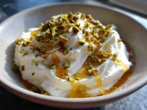 Close-up of a creamy, whipped ricotta dip drizzled with honey and topped with chopped pistachios.