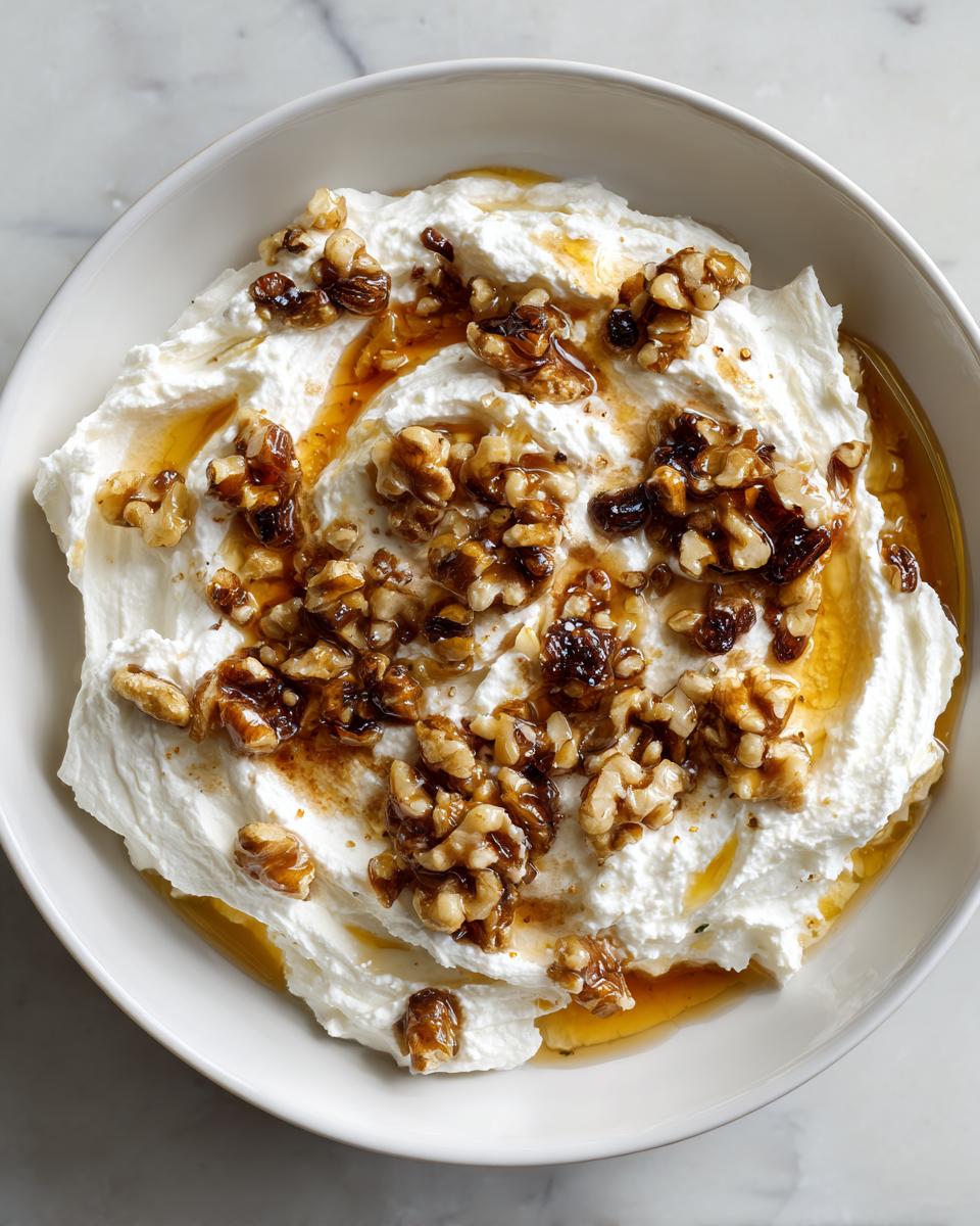 Overhead view of a bowl of creamy whipped ricotta dip topped with candied walnuts and drizzled with honey.