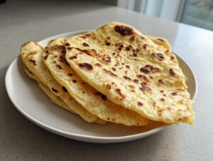 A stack of four freshly made, lightly charred corn tortillas resting on a white plate.