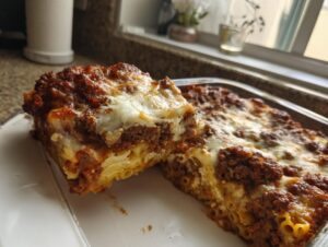 A close-up of a thick slice of baked ziti with meat sauce and melted cheese being served.