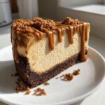 A perfect slice of creamy biscoff cheesecake topped with thick caramel drizzle and cookie crumbs.
