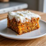 A close-up of a thick slice of amazing carrot cake bars topped with creamy white frosting on a white plate.