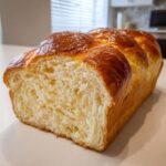 Close-up of a freshly baked loaf of condensed milk bread, showing its soft, fluffy interior and shiny, golden-brown crust.