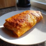 A single, golden-brown Baked Chicken Chimichanga resting on a white plate, catching bright sunlight.