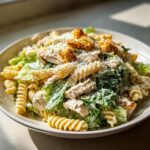A bowl of creamy chicken caesar pasta salad featuring fusilli pasta, romaine lettuce, grilled chicken, and croutons.