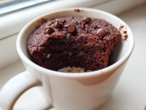 A close-up of a rich, dark chocolate Cottage Cheese Microwave Brownie topped with chocolate chips inside a white mug.