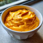 Close-up of a small white bowl filled with thick, vibrant orange beer cheese dip.