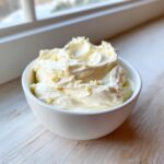 A close-up of thick, creamy homemade garlic aioli topped with visible minced garlic pieces in a white bowl.
