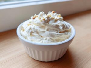 A small white ramekin filled with thick, creamy homemade garlic aioli, garnished with small specks on top.