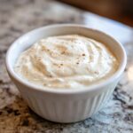 Close-up of creamy, white horseradish sauce sprinkled with spices in a small white bowl.