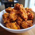 Close-up of crispy, saucy Bang Bang Chicken pieces piled high in a white bowl.
