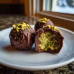 Close-up of dubai chocolate balls, one cut open revealing a bright green pistachio filling.
