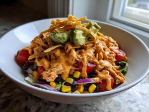A vibrant bowl of southwest salad topped with shredded chicken, avocado, tortilla strips, and creamy orange dressing.