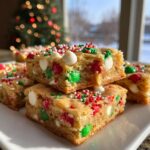 Close-up of stacked, chewy Christmas cookie bars loaded with red and green M&Ms, white chocolate chips, and holiday sprinkles.
