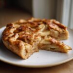 Close-up of a homemade apple galette with a slice cut out, showing layers of cinnamon apples and flaky crust.
