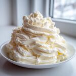 A large mound of fluffy vanilla buttercream frosting piped high in a white bowl.