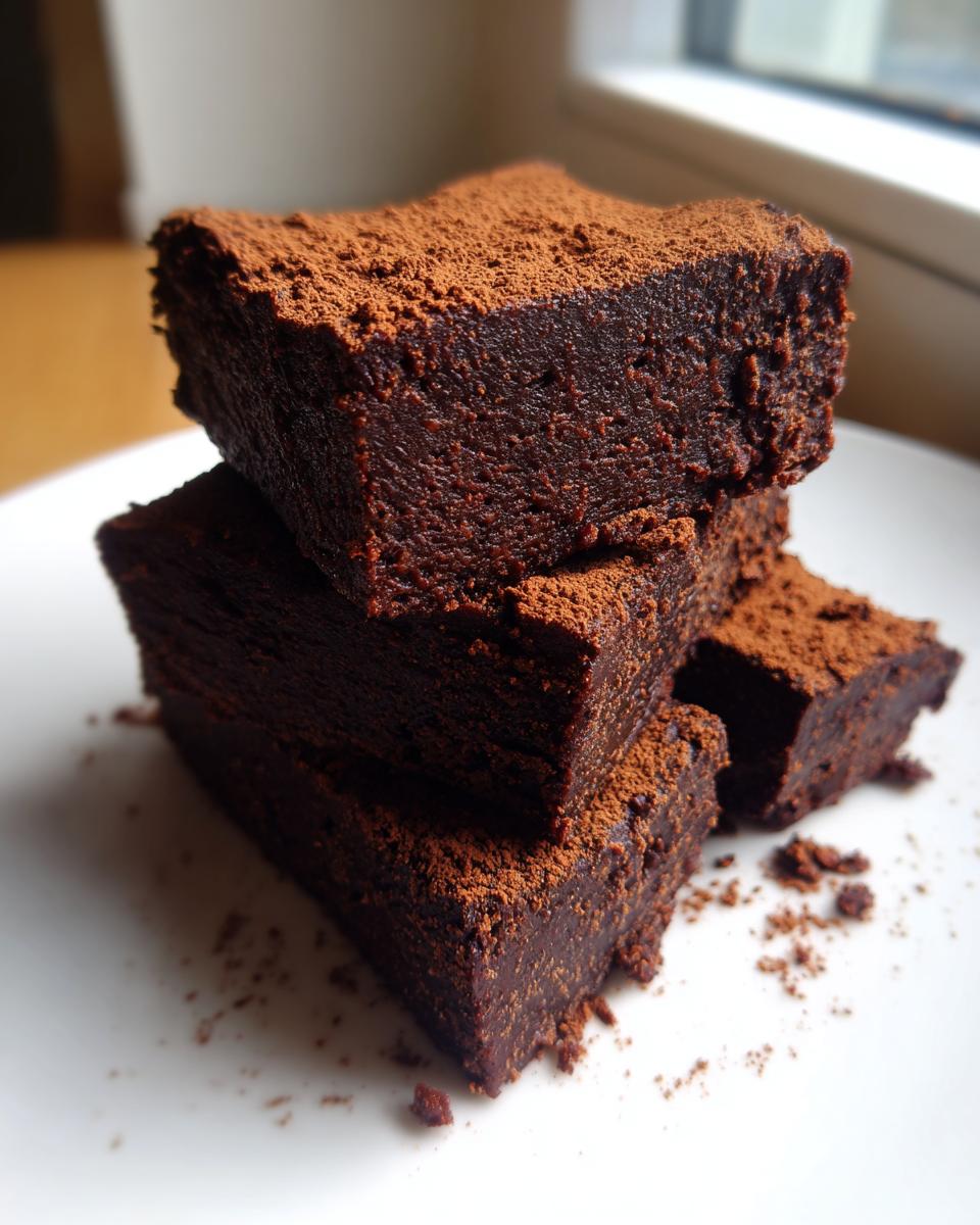 A stack of three fudgy date brownies, heavily dusted with cocoa powder, sitting on a white plate.