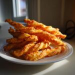 A tall stack of golden, flaky, twisted cheese straws recipe served on a white plate.