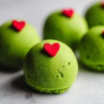 Close-up of a bright green Grinch Oreo Ball topped with a small red heart candy.