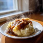 A serving of fluffy mashed potatoes generously topped with rich, steaming homemade brown gravy.