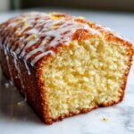 Close-up of a moist slice of olive oil cake showing the crumb texture, topped with white glaze and lemon zest.