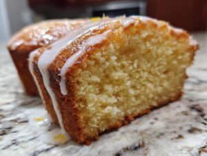 Close-up of a moist slice of olive oil cake with a thick, dripping lemon glaze and visible crumb texture.