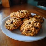 A stack of golden brown, oatmeal chocolate chip breakfast cookies piled on a white plate.
