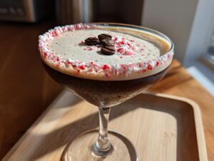A close-up of a festive peppermint espresso martini garnished with a candy cane rim and coffee beans.