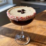 A festive peppermint espresso martini with a crushed candy cane rim and coffee bean garnish.