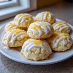 A pile of soft italian ricotta cookies drizzled with white glaze and topped with lemon zest.