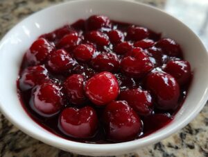 Close-up of thick cherry pie filling, featuring glossy, whole cherries suspended in rich, dark red sauce.