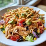 Close-up of a vibrant southwest salad featuring shredded chicken, avocado, black beans, corn, and crispy tortilla strips.